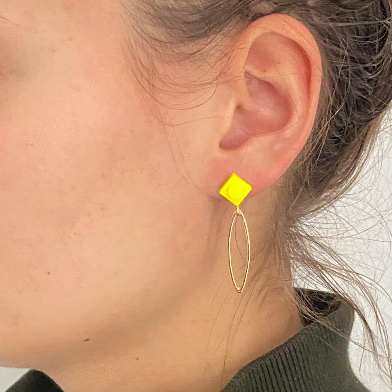 Boucle d'oreilles pendante avec un oval en laiton doré suspendue à une brique de Lego 1x1 plate jaune fluo. Elle se coordonne parfaitement avec un pull vert kaki. 